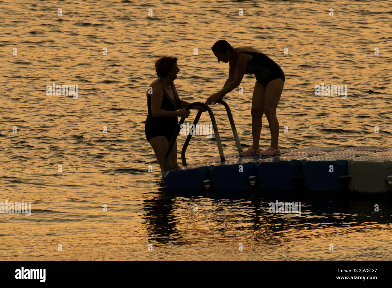 Two Ladies Swimming At Sunset At Aegean Sea. Stock Photo