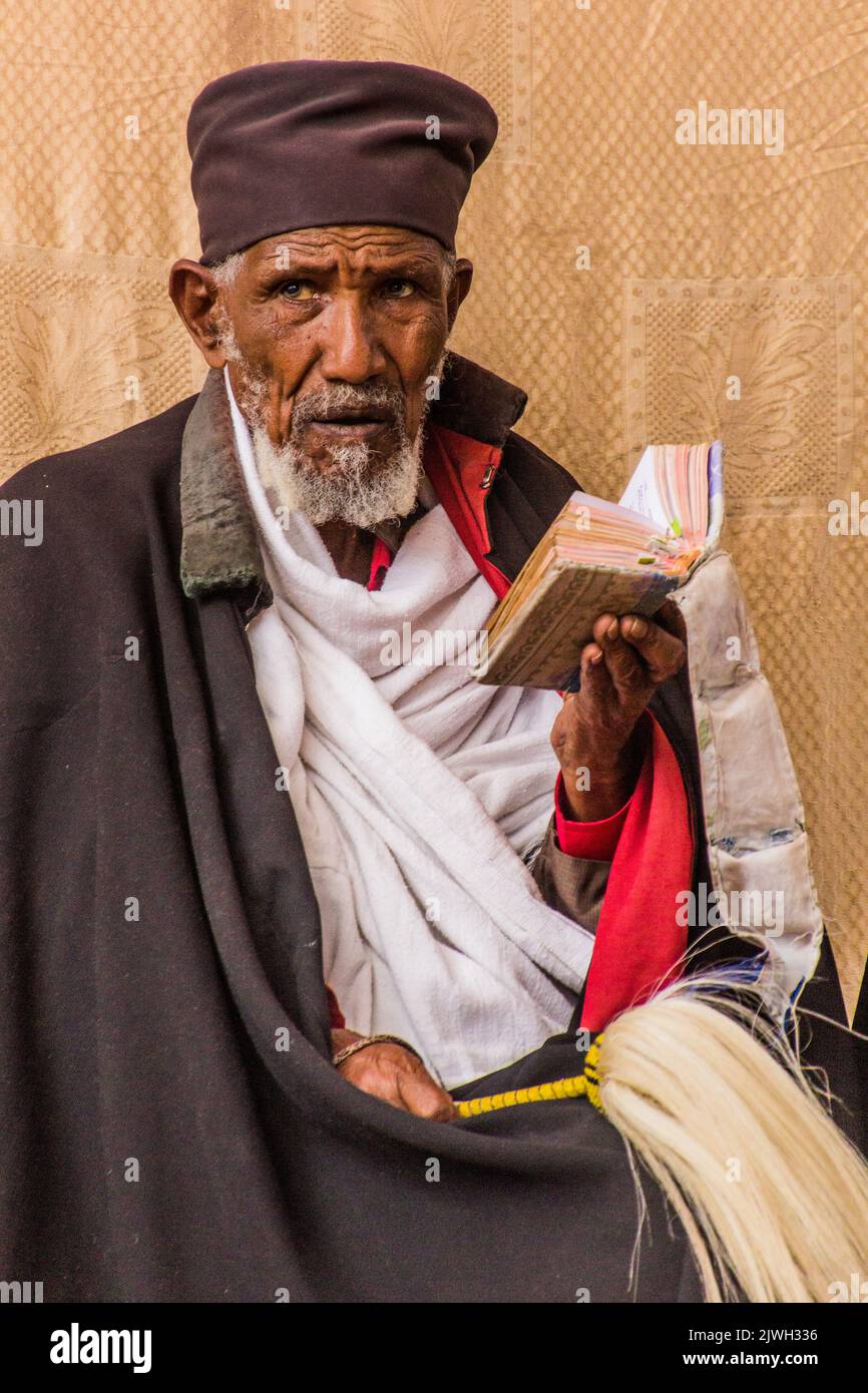 LALIBELA, ETHIOPIA - MARCH 29, 2019: Christian priest reading a Bible in front of Bet Maryam, rock-cut church in Lalibela, Ethiopia Stock Photo