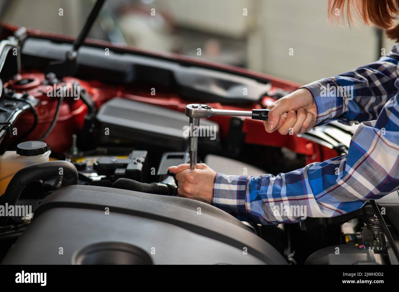 Female auto mechanic unscrewing a nut to replace a car spark plug Stock