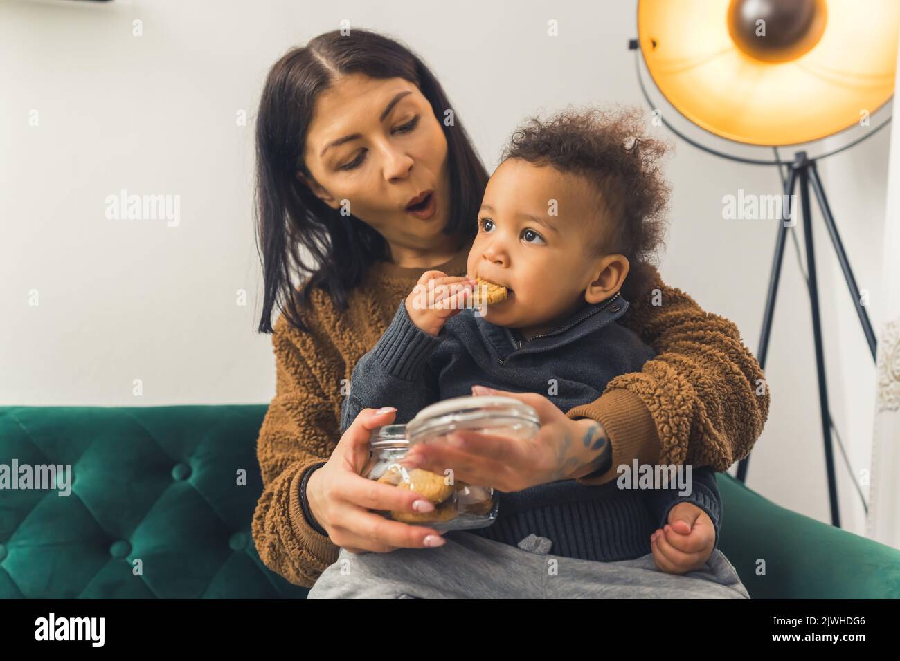 cute little boy sitting in his mother's lap and eating a cake, medium shot family concept home. High quality photo Stock Photo