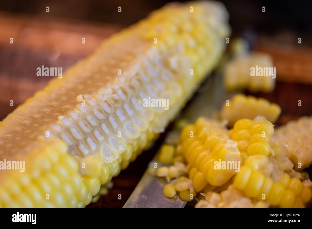 Using a knife to remove kernels from the cob of an ear of sweet corn