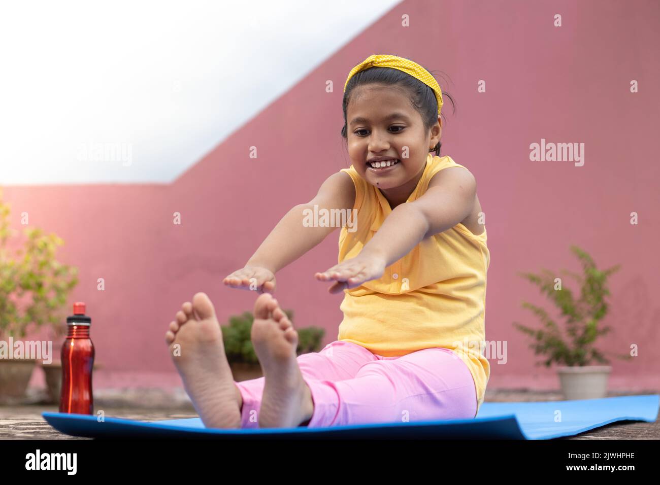An Indian girl child practicing yoga on yoga mat outdoors Stock