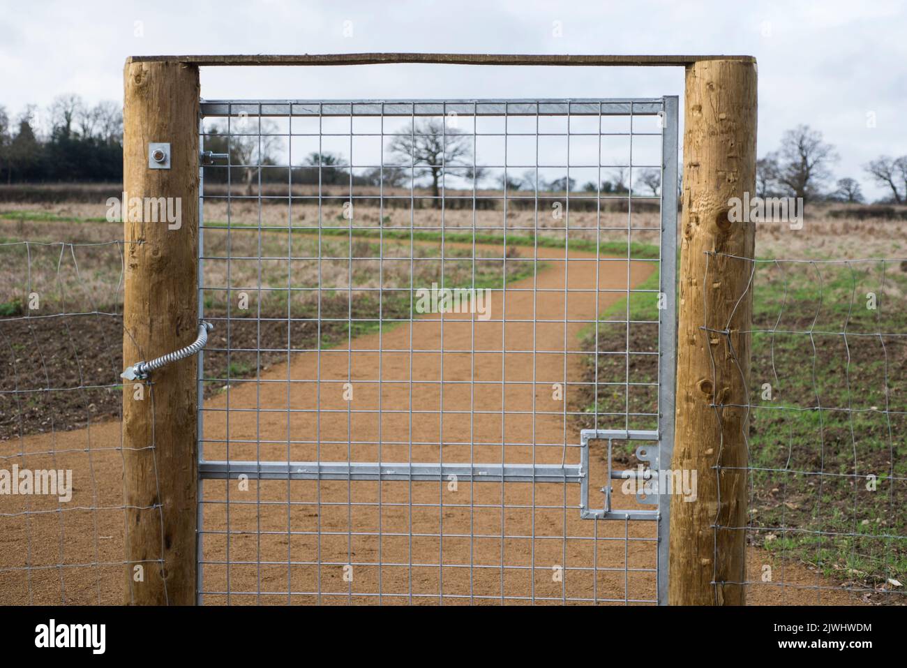 A brand new galvanised steel gate with wooden fence posts and new gravel walking pathway beyond it in a rural area of north London England UK Stock Photo