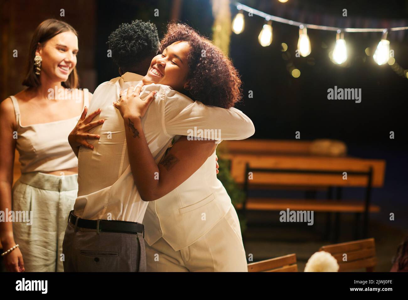 Young cheerful African American bride giving hug to black man in white shirt while meeting guests coming to wedding party and feast Stock Photo