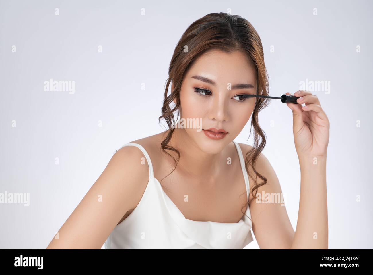 Gorgeous young woman putting black mascara on her long eyelashes with brush. Beauty cosmetic concept. Female model with perfect skin. Stock Photo