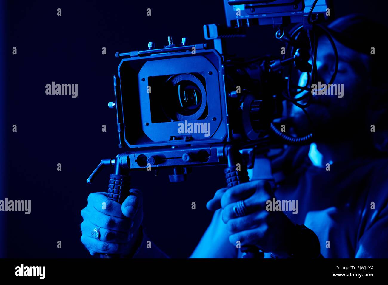 Hands of young videographer or photographer holding by handles on tripod on steadicam while shooting commercial in darkness Stock Photo