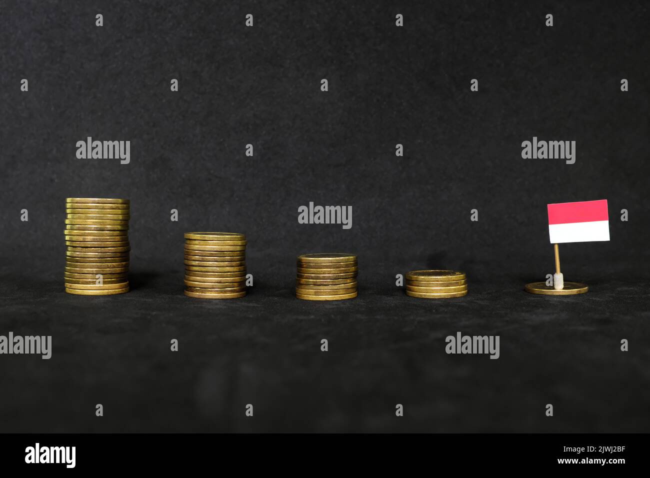 Indonesia economic recession, financial crisis and currency depreciation concept. Indonesian flag in decreasing stack of coins in dark black Stock Photo