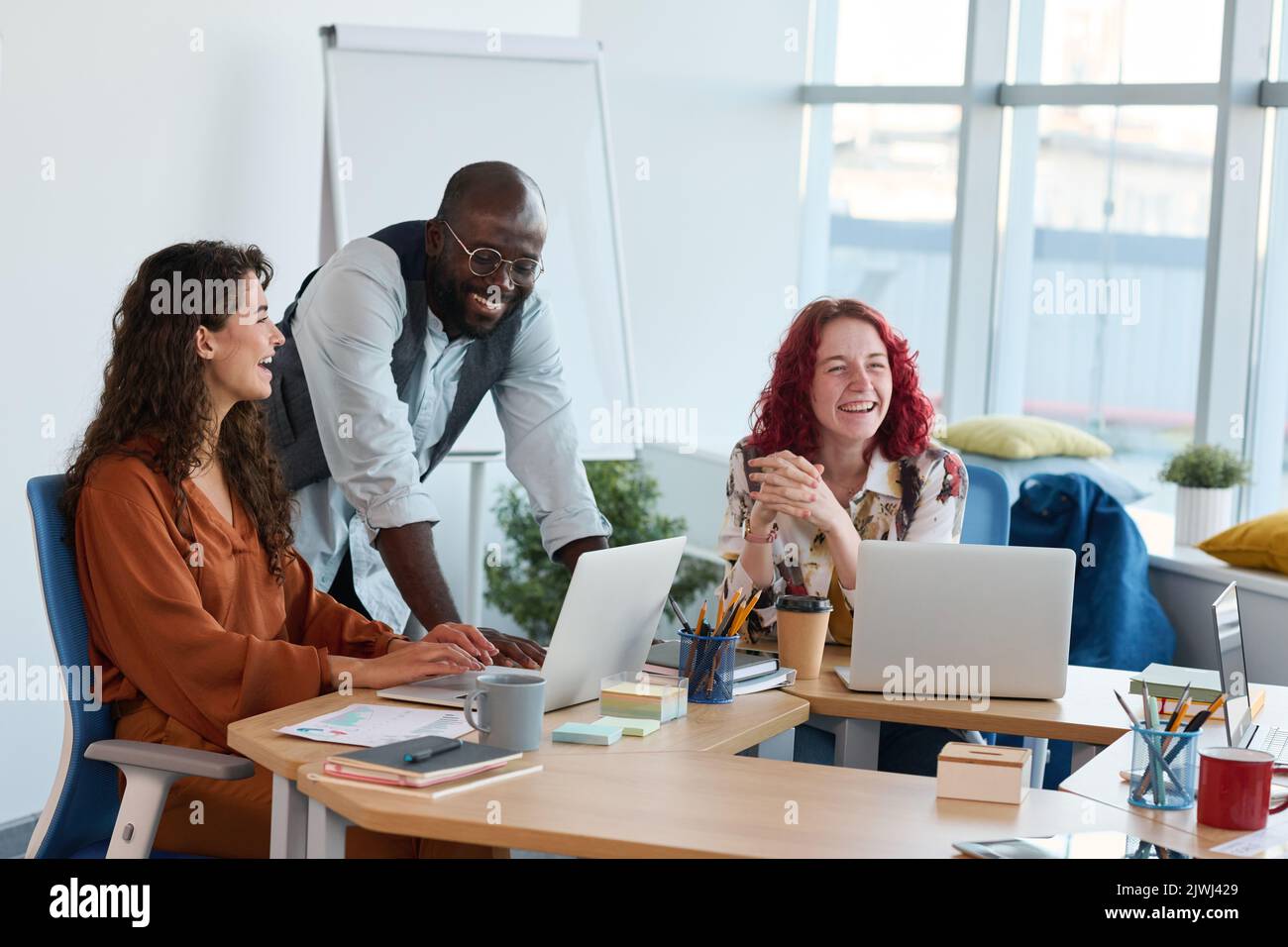 Three young multicultural employees laughing at working meeting in office during discussion of new ideas or points of project Stock Photo