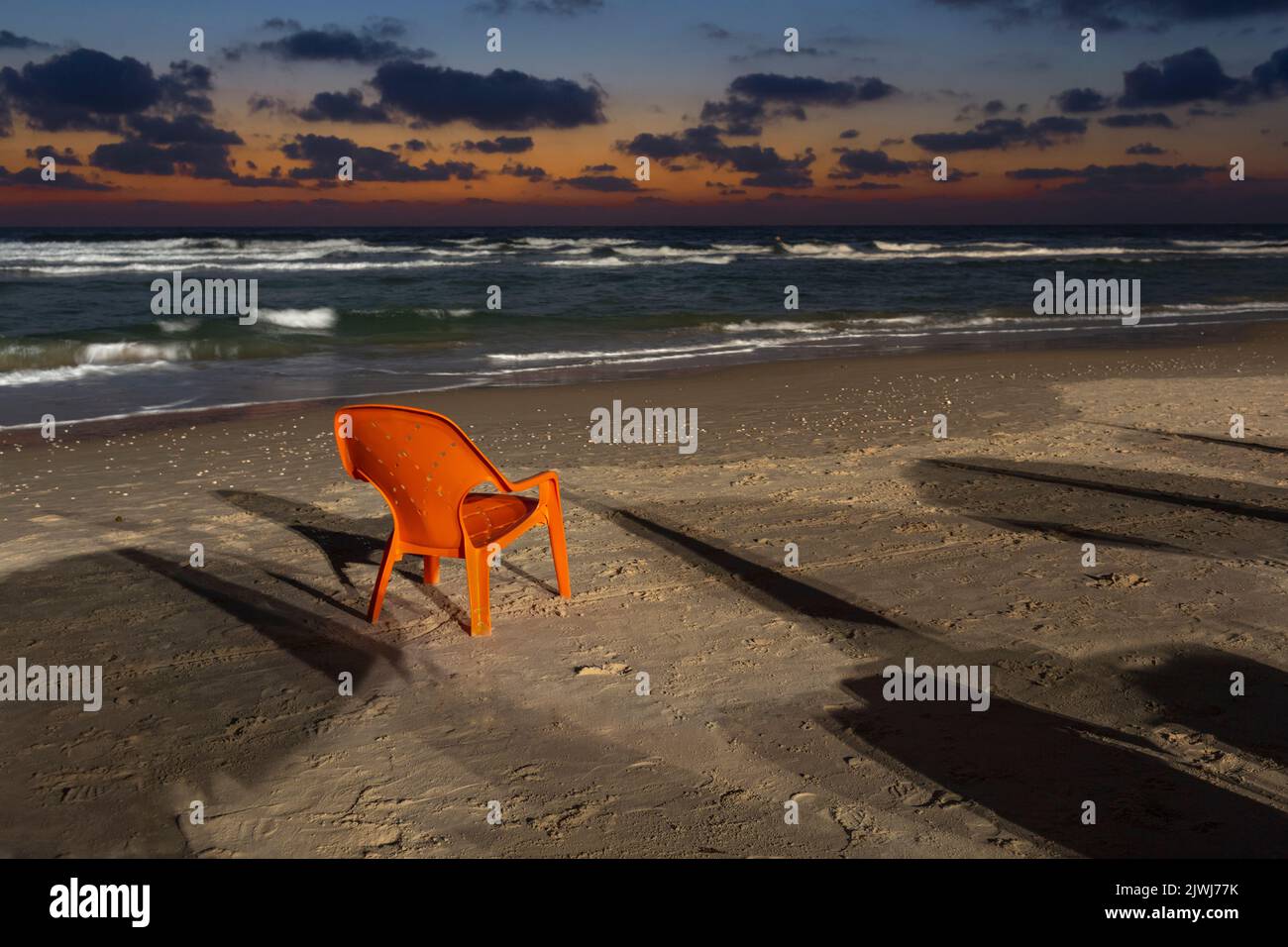 Orange lawn chair on sandy beach at dusk, Bat Yam, Israel Stock Photo