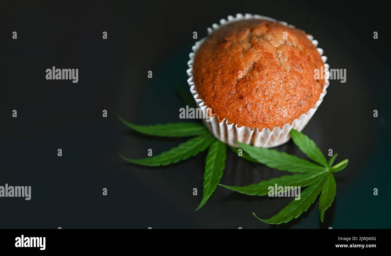 Cannabis food cake with cannabis leaf marijuana herb on dark background, delicious sweet dessert cupcakes with hemp leaf plant THC CBD herbs food snac Stock Photo
