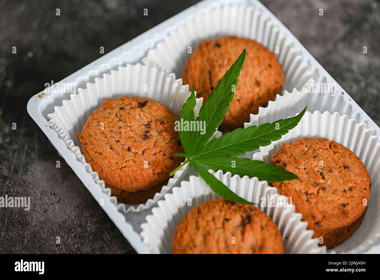 Cannabis food cookies box with cannabis leaf marijuana herb on dark background, delicious sweet dessert cookie with hemp leaf plant THC CBD herbs food Stock Photo