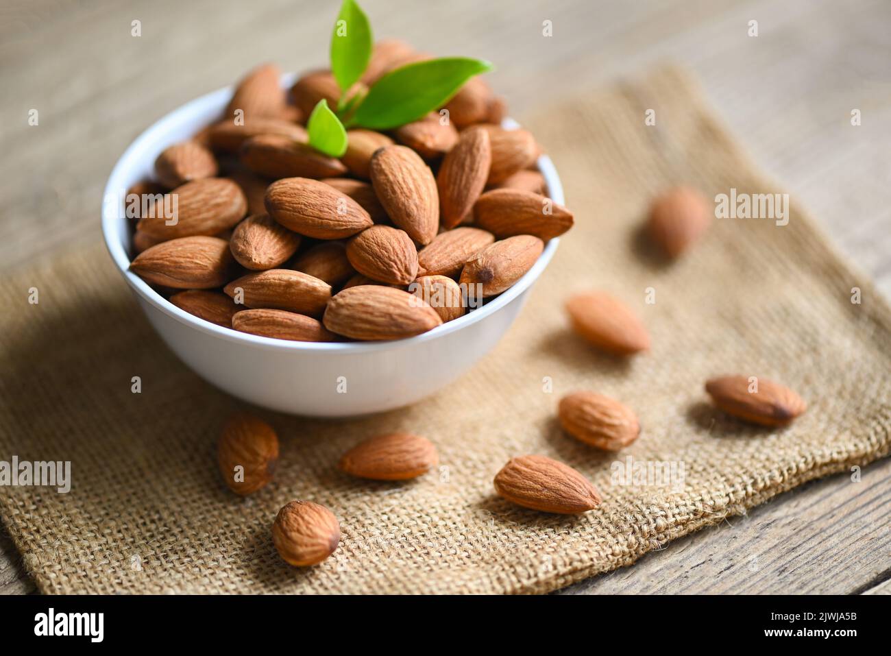 Almonds nuts on white bowl and green leaf on sack backgroundม, Delicious sweet almonds on the wooden table, roasted almond nut for healthy food and sn Stock Photo