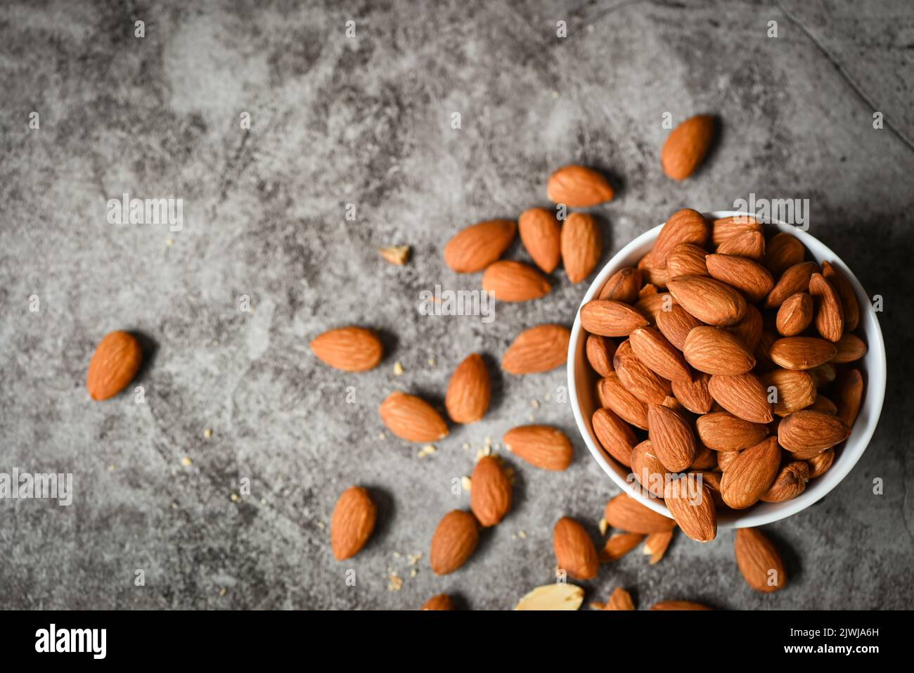 Almonds nuts on white bowl, Delicious sweet almonds on the table dark background, roasted almond nut for healthy food and snack Stock Photo