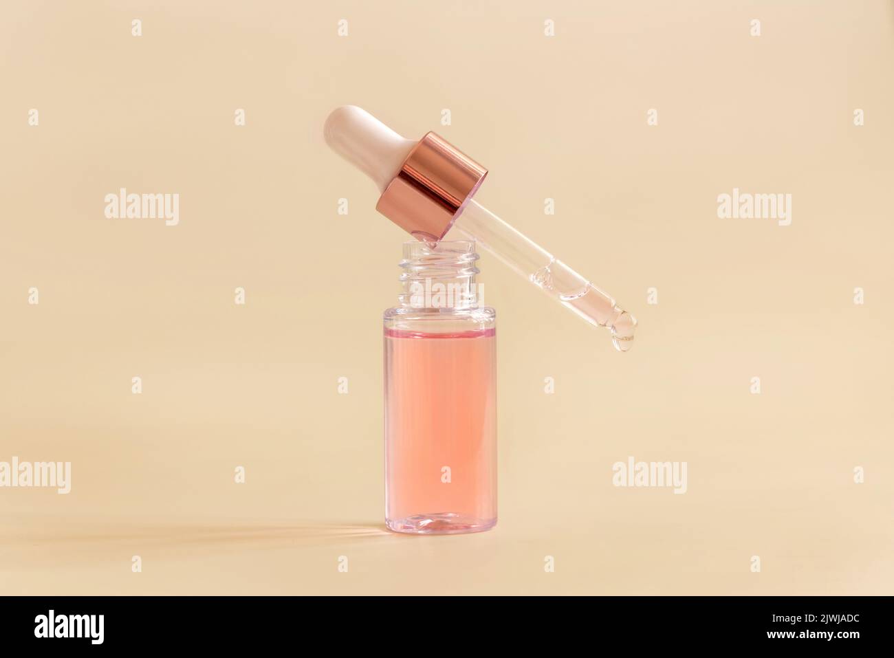 Opened Bottle with serum drop falling from pipette cap on light beige