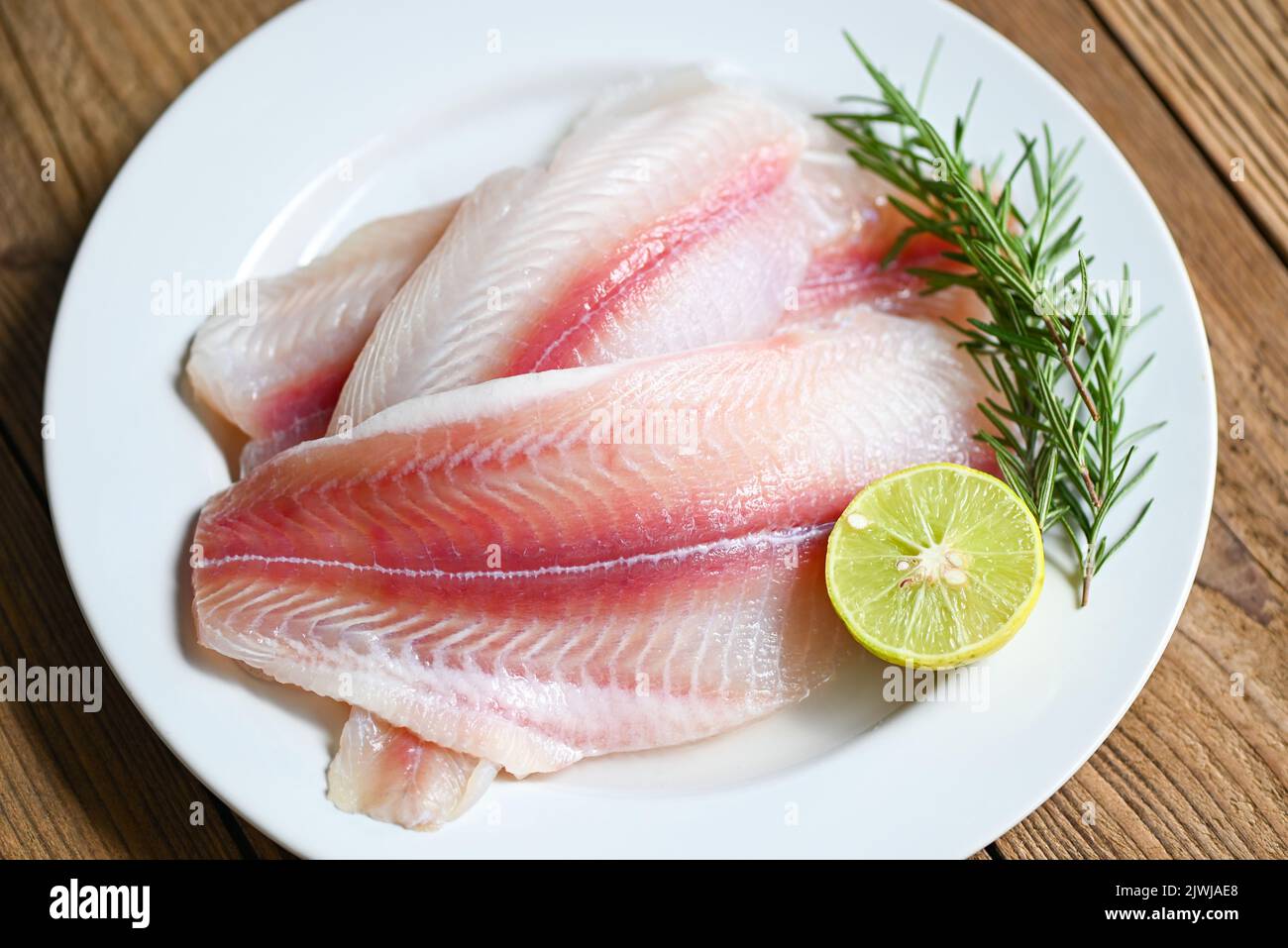 fish fillet on white plate with ingredients for cooking, fresh raw pangasius fish fillet with herb and spices lemon lime and rosemary, meat dolly fish Stock Photo