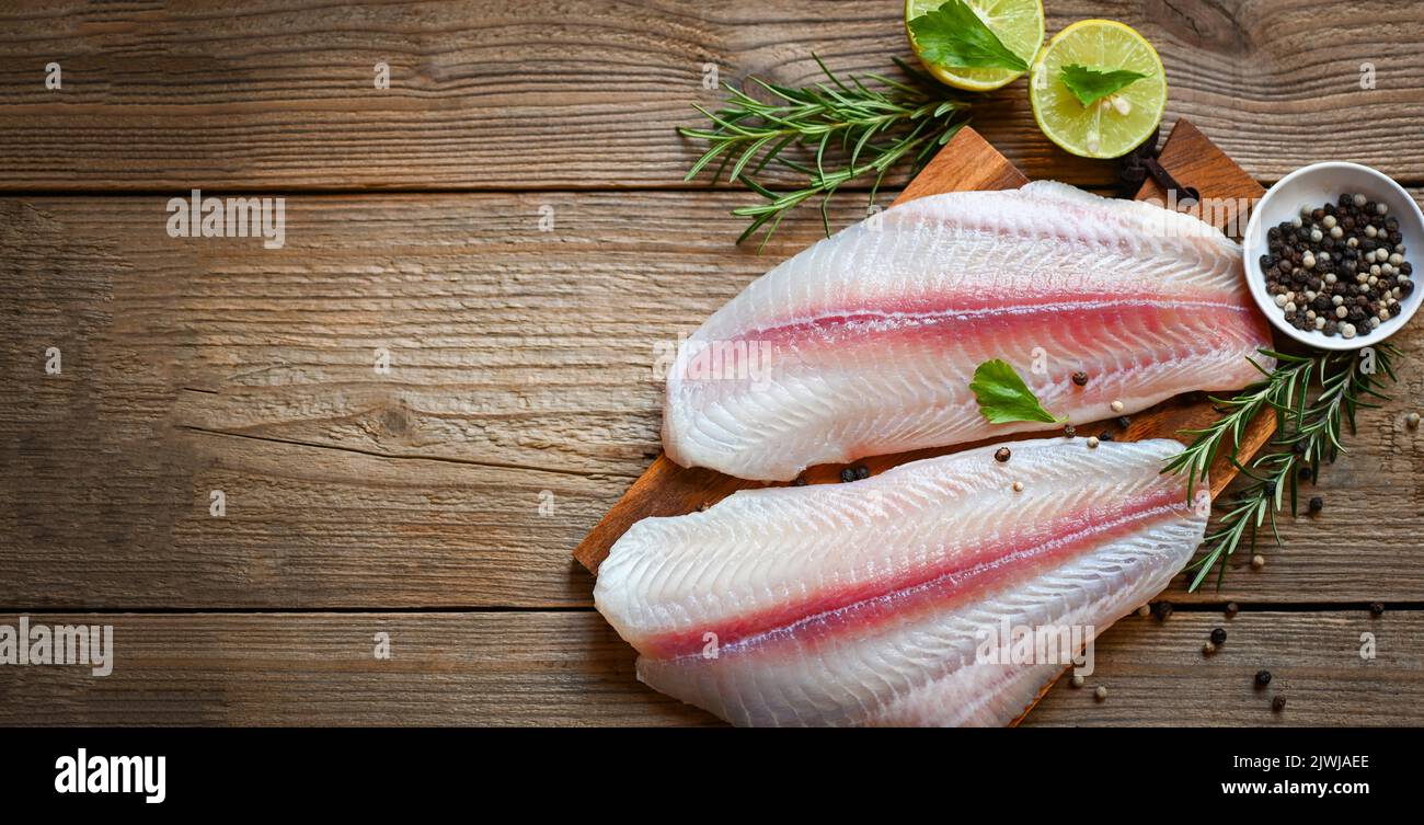 fresh raw pangasius fish fillet with herb and spices black pepper lemon lime, fish fillet on wooden board with ingredients for cooking, meat dolly fis Stock Photo