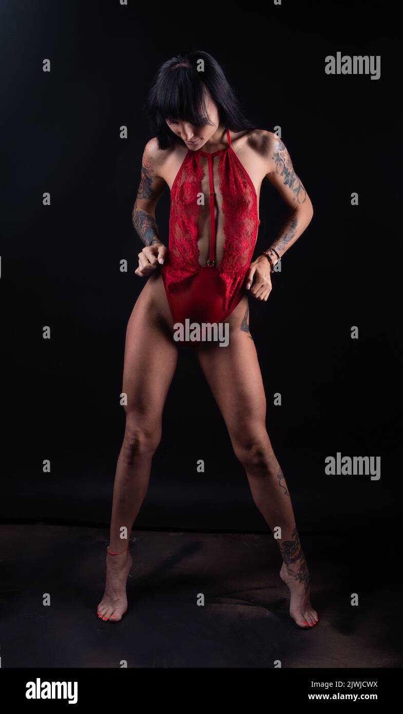 Photo of brunette woman with tattoo in red lingerie on dark background Stock Photo