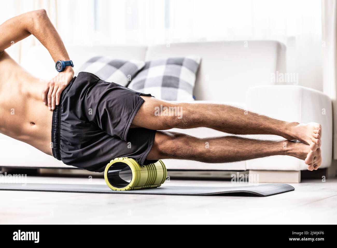 Young man massage lateral thigh muscle with foam roller. Stock Photo