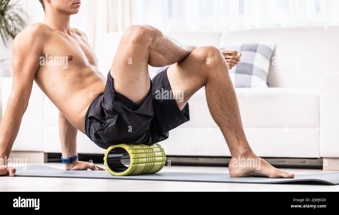 A young man massages the gluteal muscle with a foam roller. Stock Photo