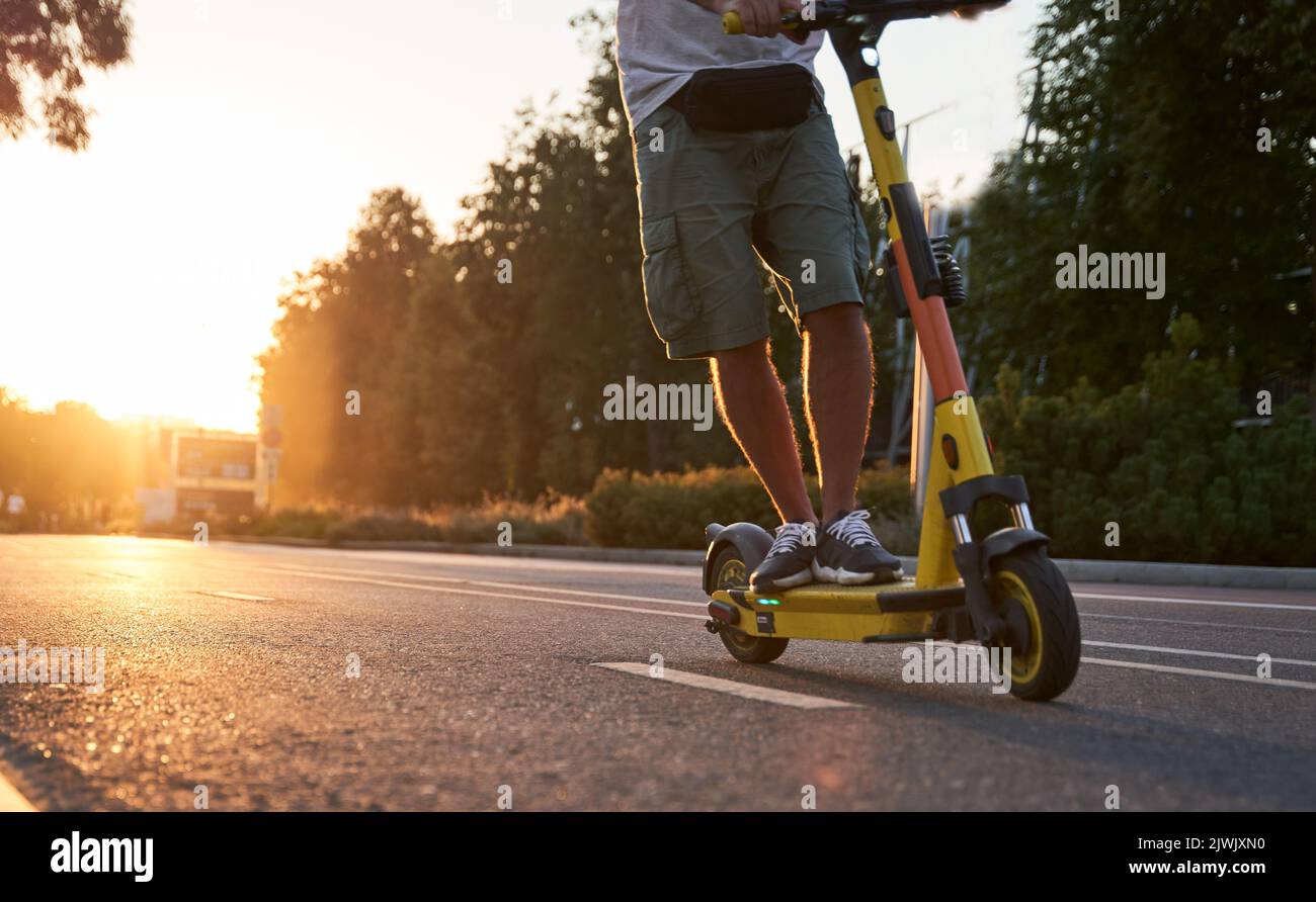Man is riding on electric scooter or escooter on the street on the sunset. Electric urban