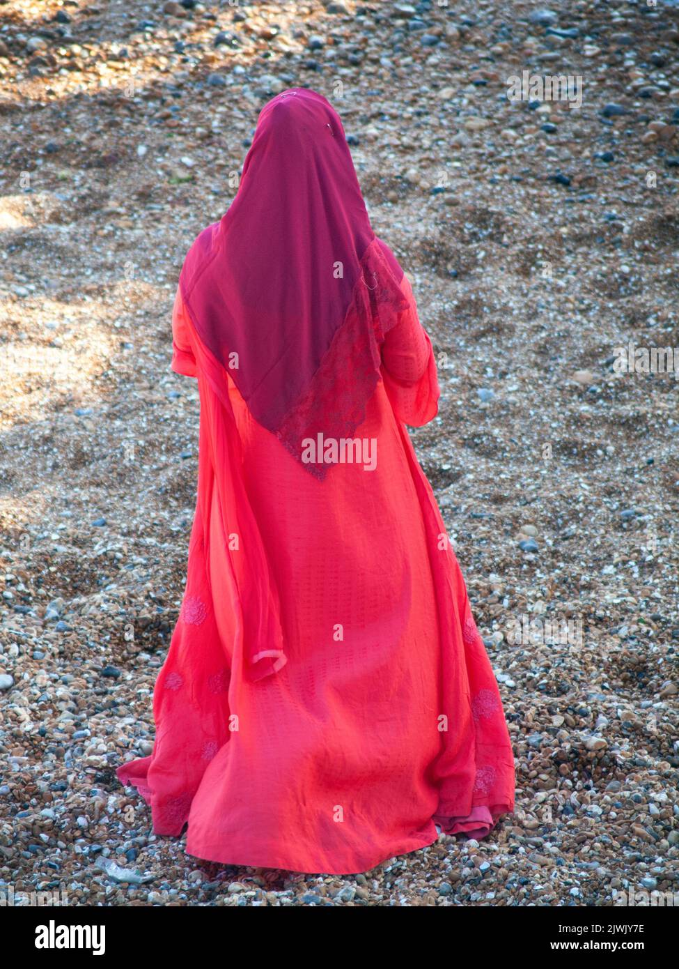 On the beach at Brighton a woman wears a bright red item of Islamic clothing Stock Photo