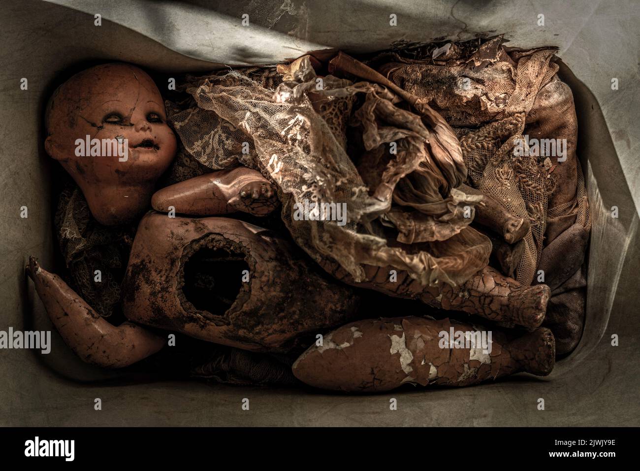 Dirty and damaged doll covered by rags inside a box. Scary Baby Doll. Disturbing horror movie concept for dark mood Stock Photo