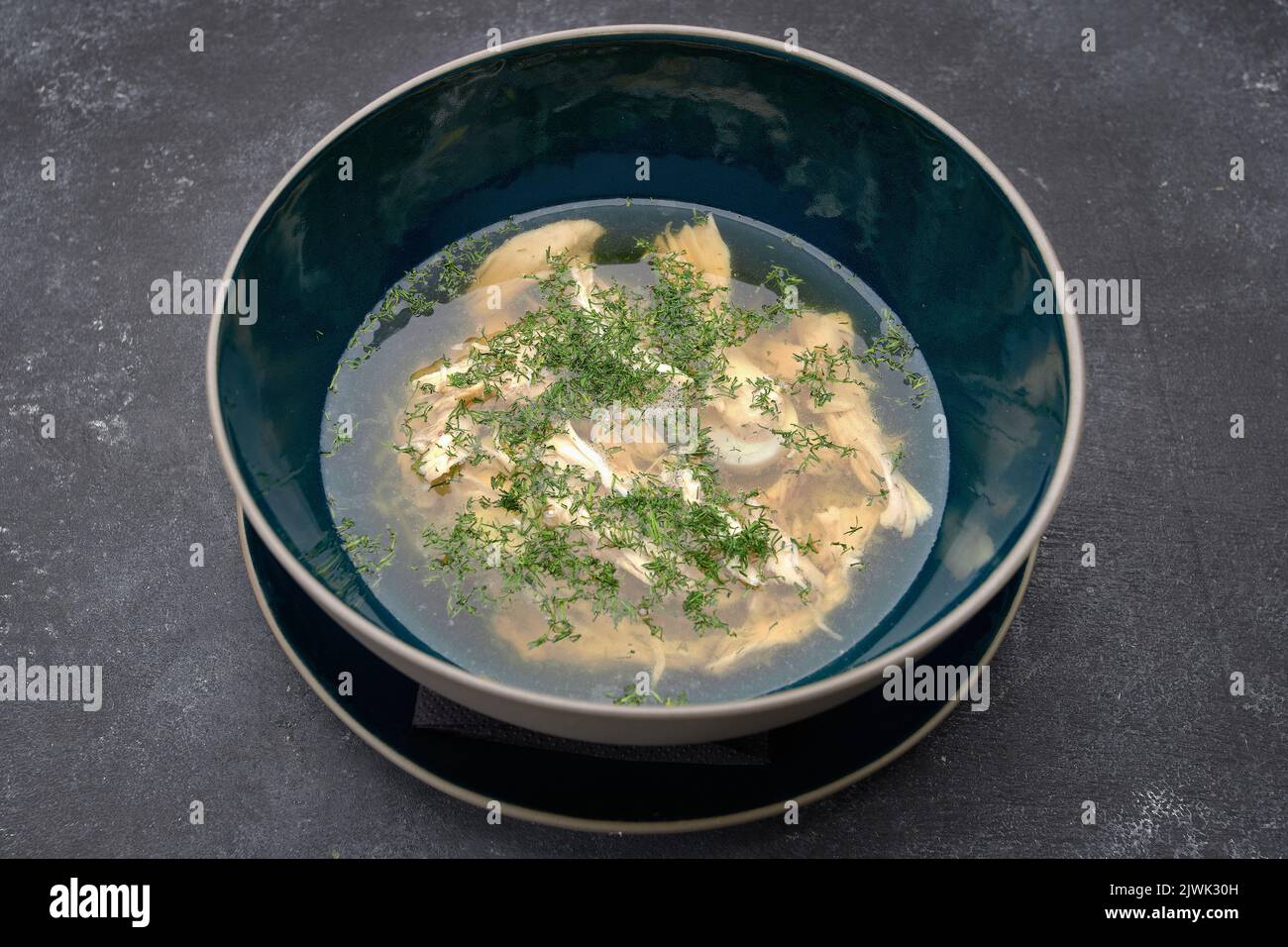 Transparent chicken broth with dill, consomme, on a dark background