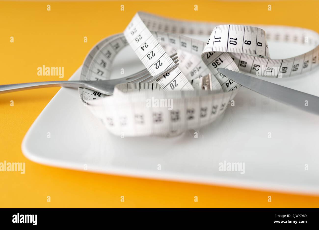 tape measure on plate with fork and knife against orange table background, dieting and loosing weight concept Stock Photo