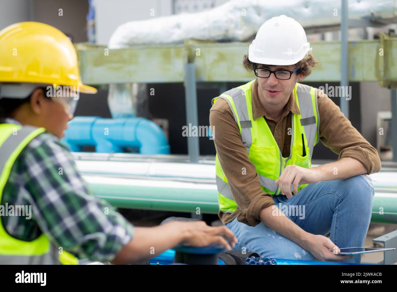 Young woman and man engineer examining pipeline and talking in the factory, mechanic or technician inspector and check plumber valve and discussion to Stock Photo