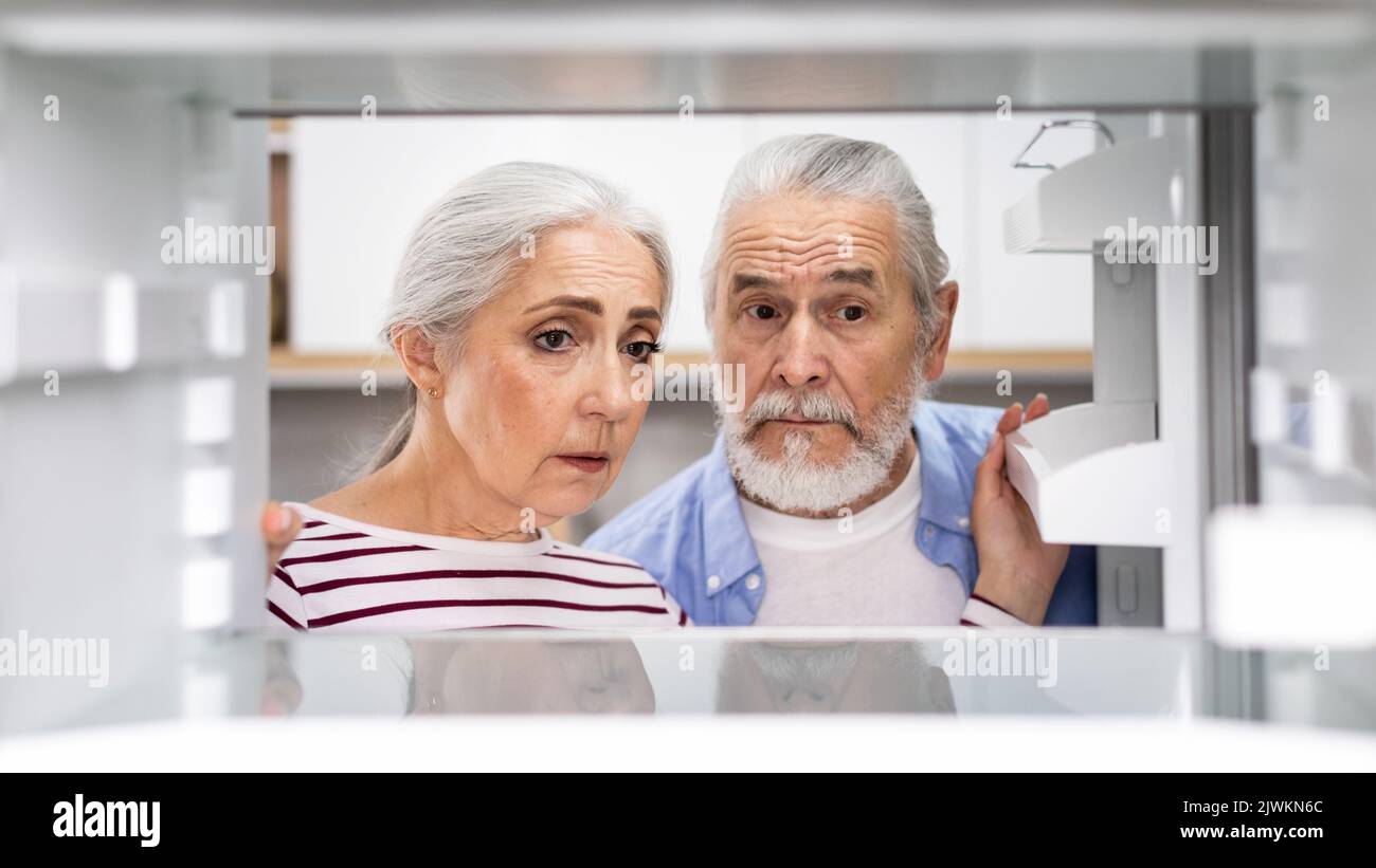 Crisis And Poverty. Upset Senior Couple Looking At Empty Shelves In Fridge Stock Photo