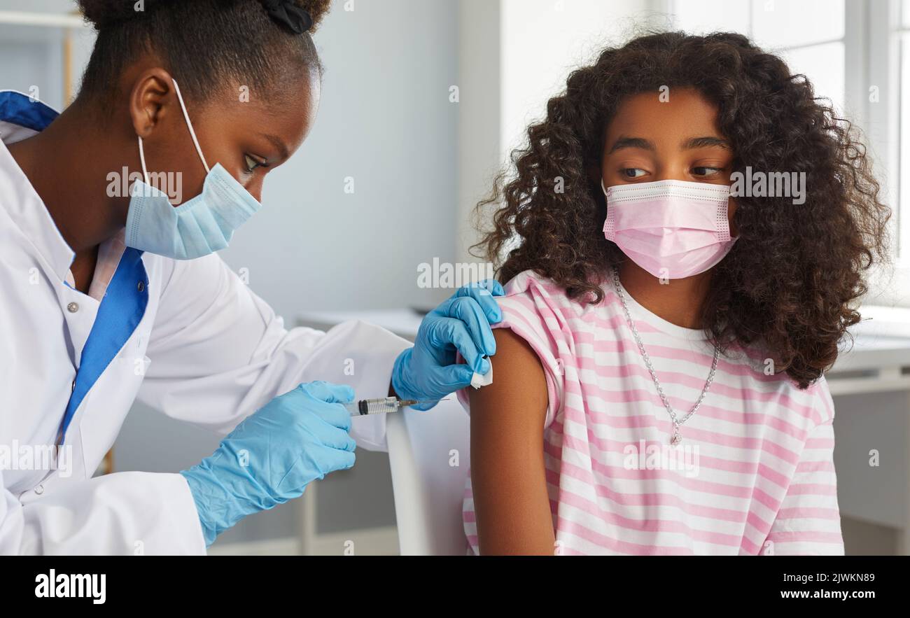 Brave African American teenage girl receives booster dose of coronavirus vaccine. Stock Photo