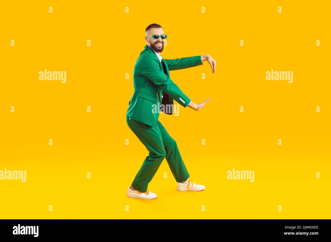 Side view of a funny man in a green party suit dancing isolated on a yellow background Stock Photo