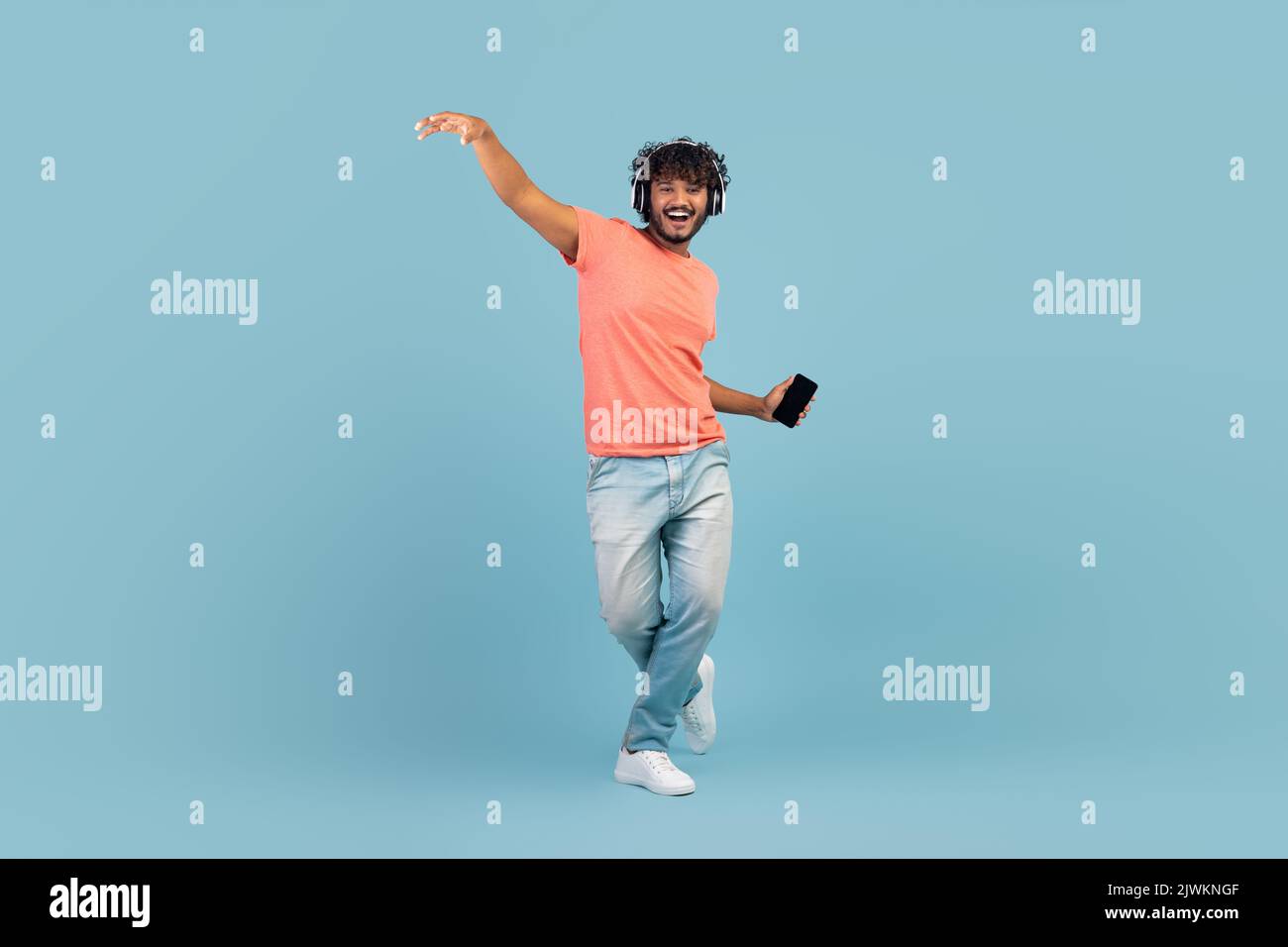 Happy eastern guy using wireless headset and smartphone, dancing Stock Photo