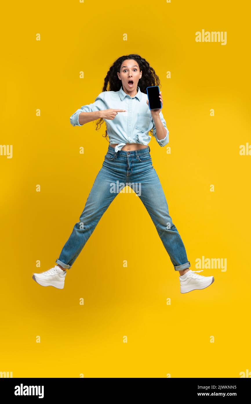 Shocked Lady Showing Smartphone Empty Screen Jumping Over Yellow