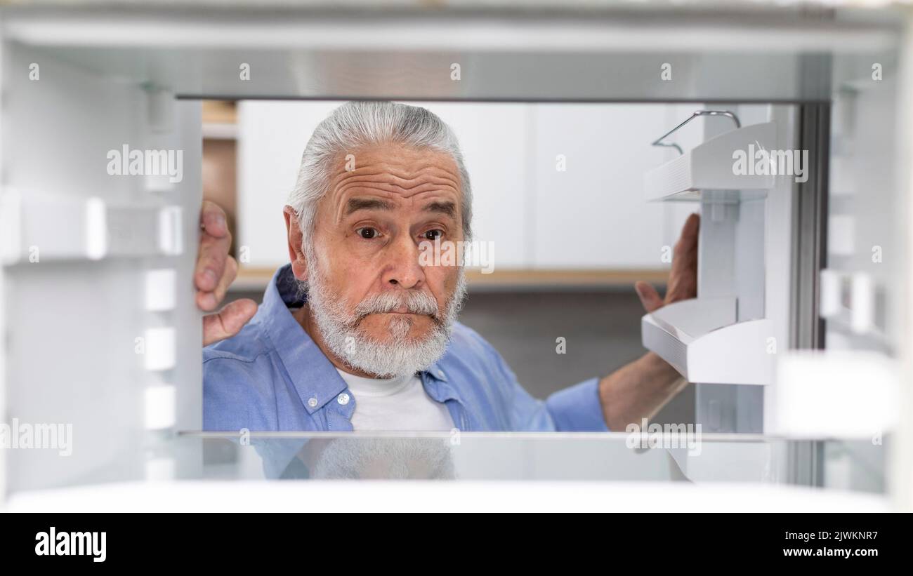 Hungry Senior Man Looking At Empty Shelves In Fridge At Home Stock Photo
