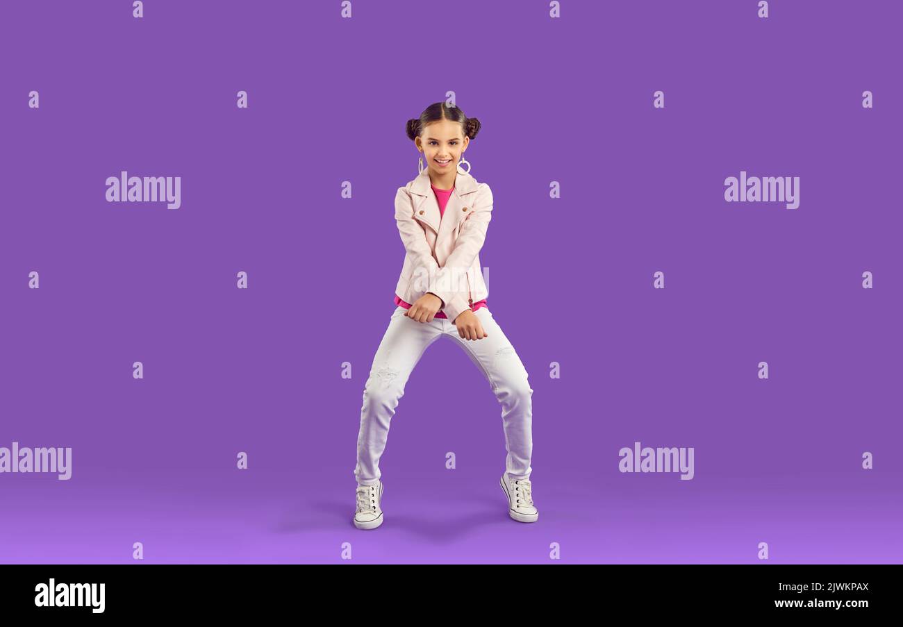 Young positive Caucasian girl teen performs fashionable modern dance stands on purple background Stock Photo