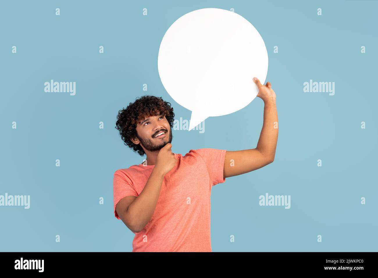 Pensive indian man holding blank speech bubble on blue, thinking Stock Photo