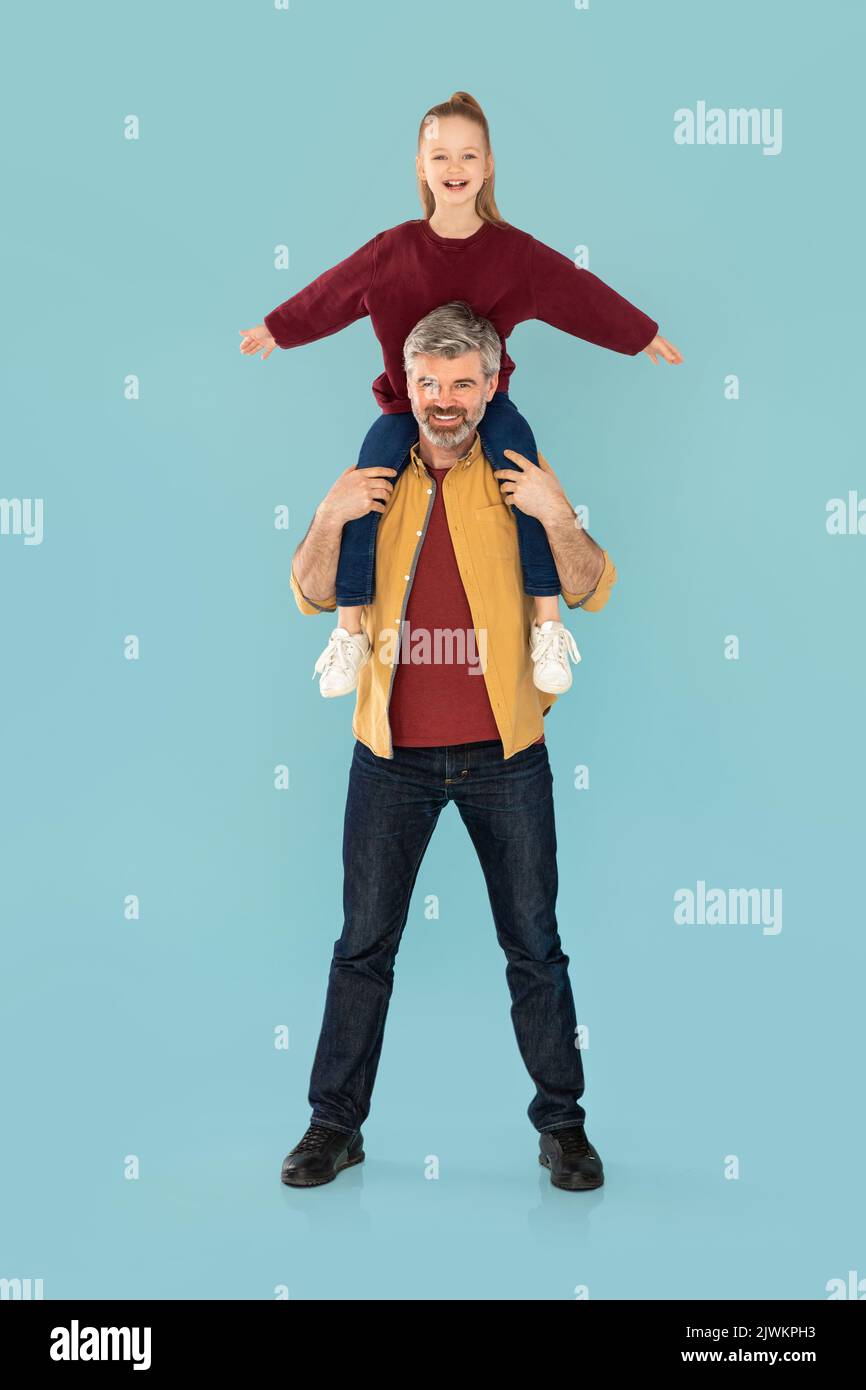 Middle Aged Dad Holding Kid Daughter On Shoulders, Blue Background Stock Photo