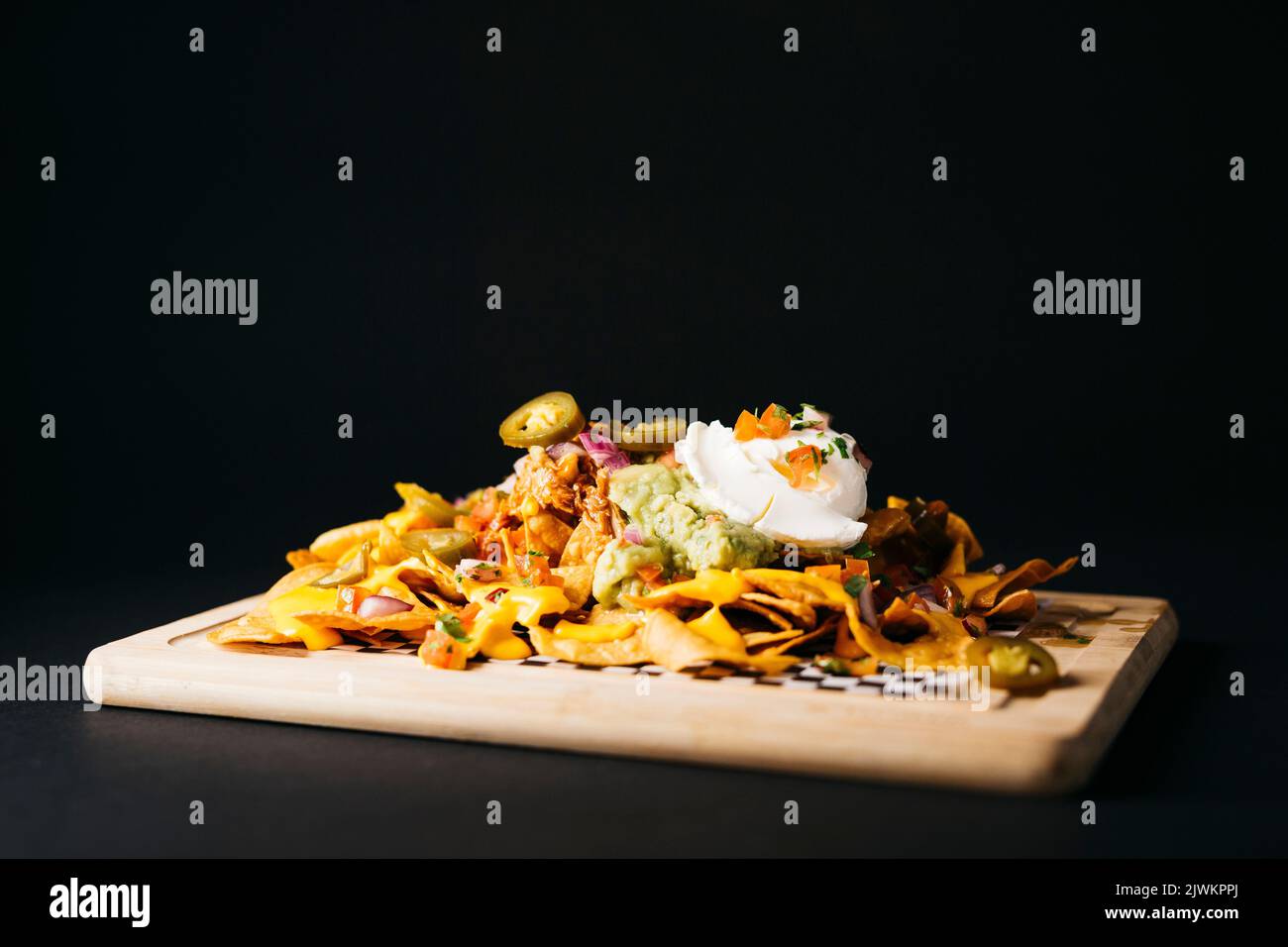 Nachos topped with melted cheese and other savory toppings over a black background Stock Photo