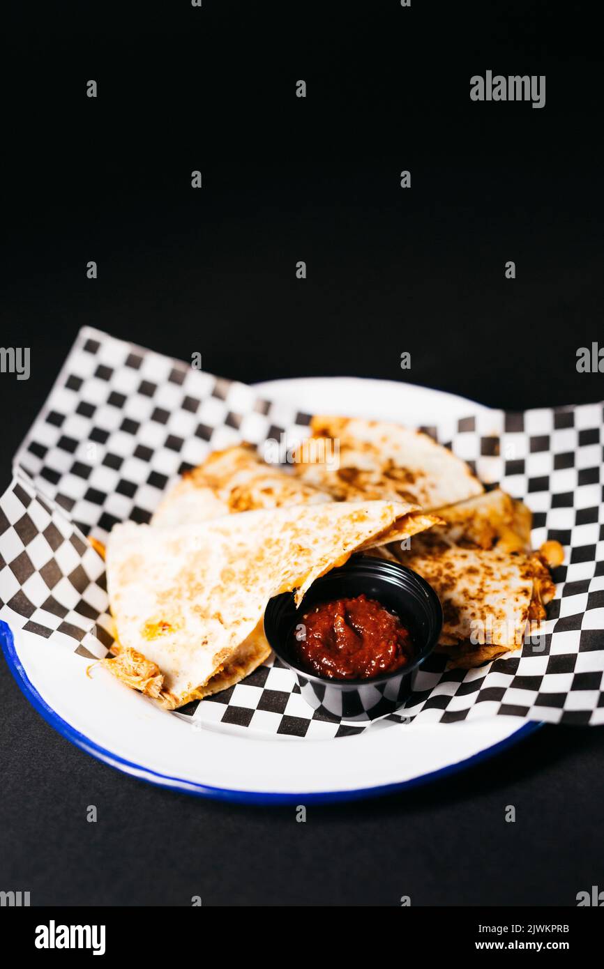 Pulled chicken Quesadilla accompanied with a spicy tomato sauce over a black background Stock Photo