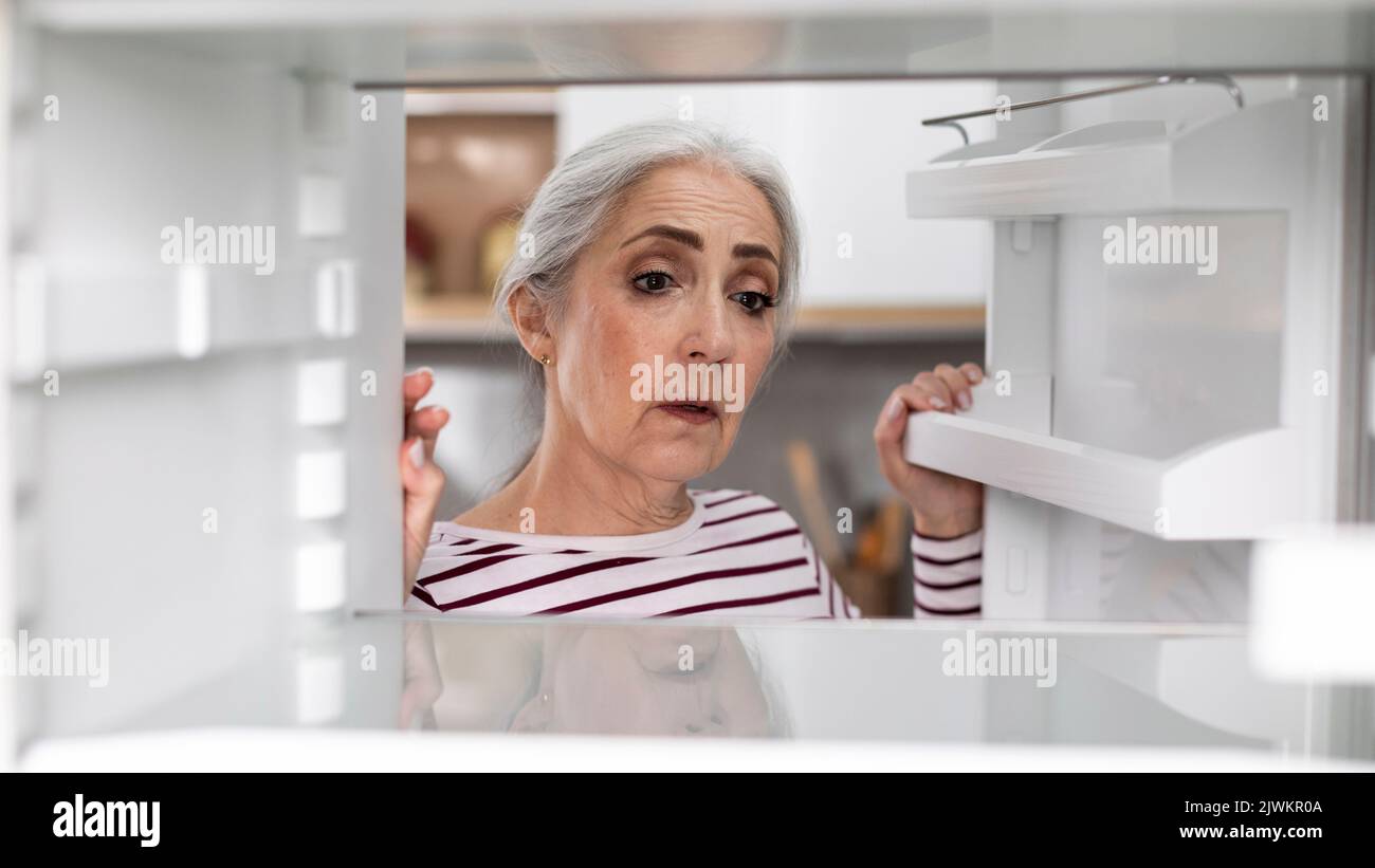 Sad Senior Woman Looking At Empty Shelves In Fridge At Home Stock Photo
