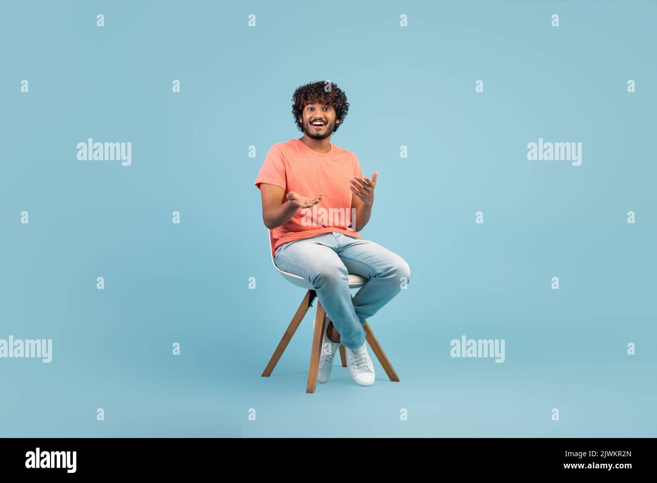 Cheerful eastern guy sitting on chair over blue background Stock Photo