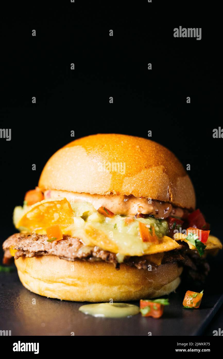 Doble burger with nachos, chopped tomatoe and guacamole sauce over a black background Stock Photo