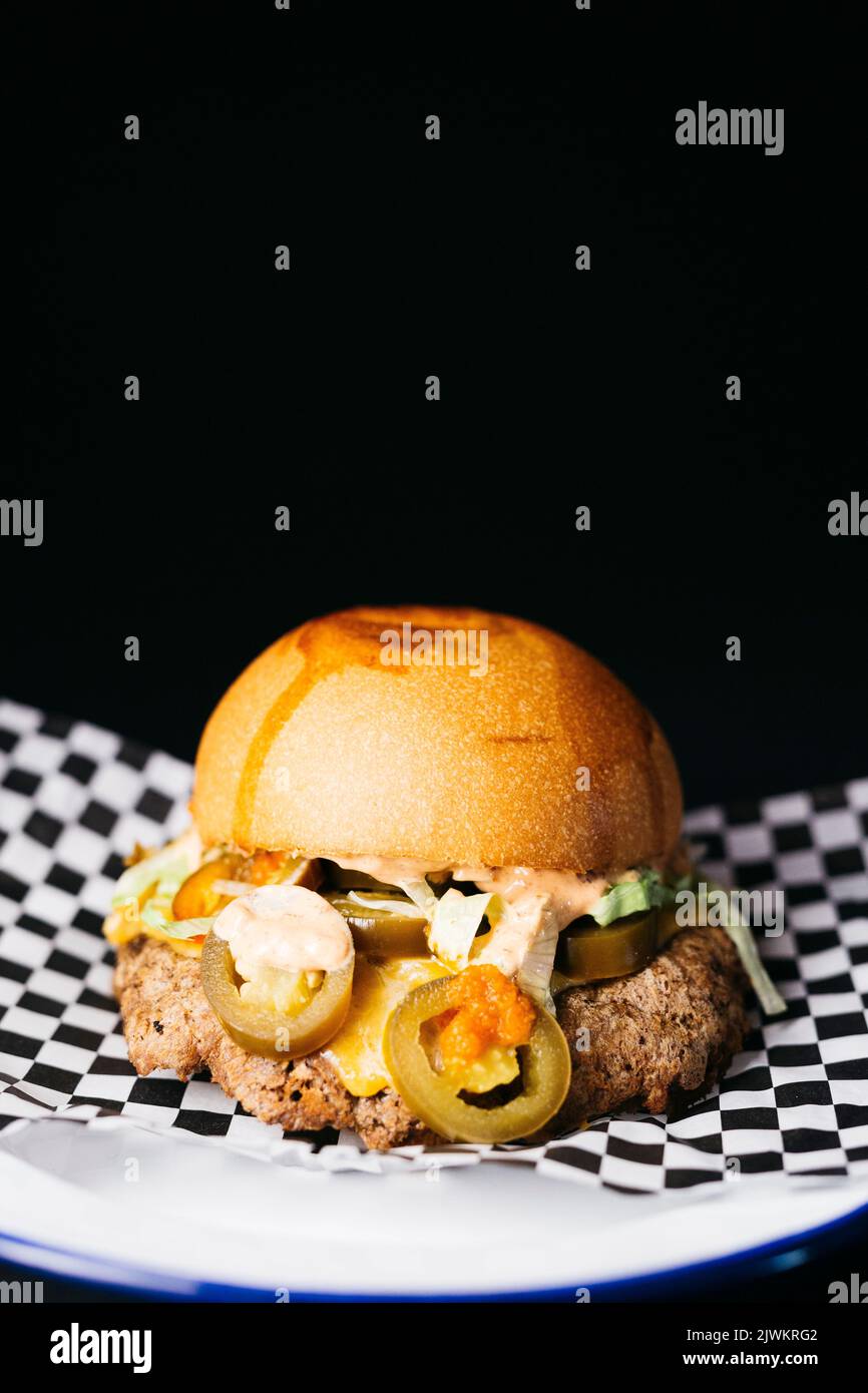 Doble cheeseburger with vegetables and jalapeños on a white plate over a black background Stock Photo