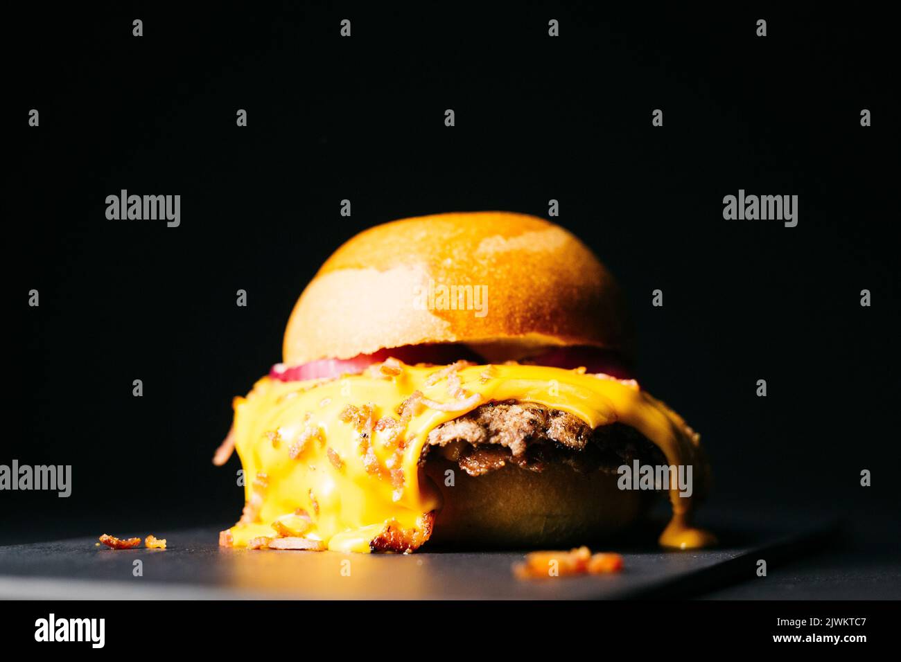 Doble burger with melted cheese and topped with bacon over a black background Stock Photo