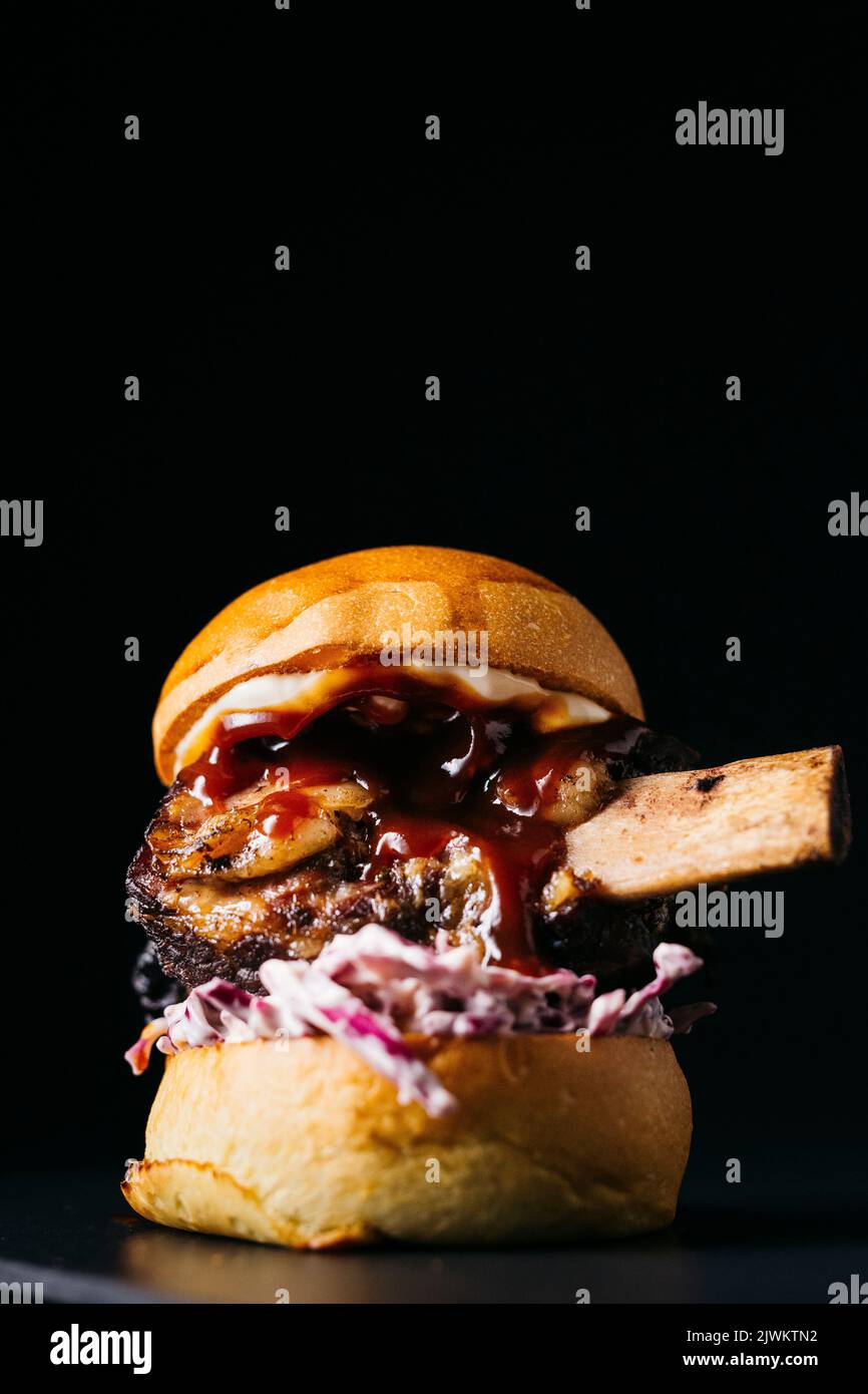Beef rib burger and it's bone on a white plate on a wooden table over a black background Stock Photo
