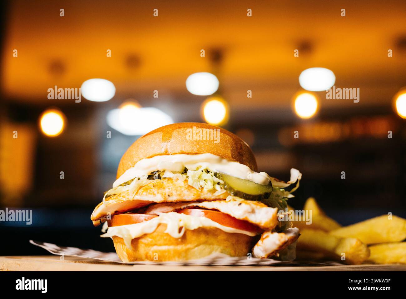 Close up of a chicken burger with cheese on a wooden table in a restaurant Stock Photo