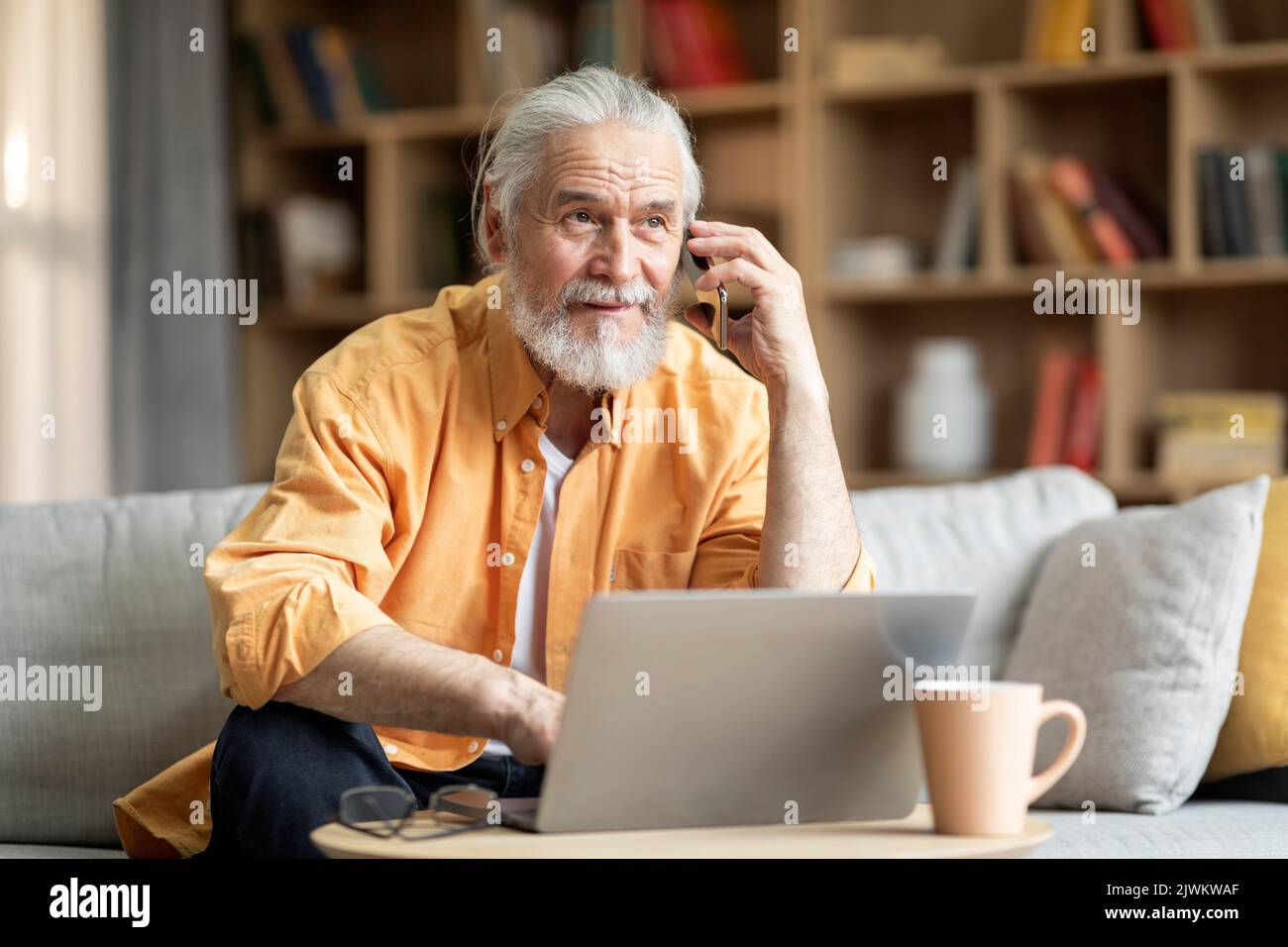 Cheerful elderly man using laptop, having phone conversation Stock Photo