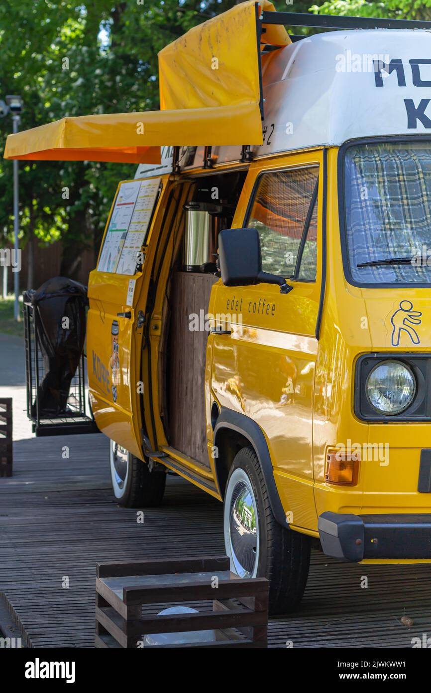 yellow retro mini bus car van parked in city park, used as stall for selling coffee. Fun vehicle for snack delivery sale journey. roadtrip on yellow v Stock Photo