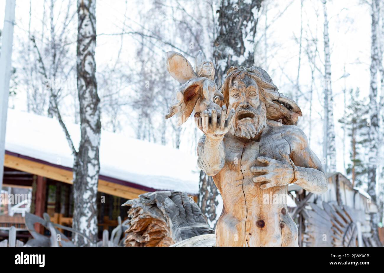 Siberian traditional wooden figurine. old wooden sculpture in the forest, Centaur holding a forest fairy in his hand. Siberia, Park Outskirts. Carved Stock Photo